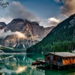 mirror lake reflecting wooden house in middle of lake overlooking mountain ranges